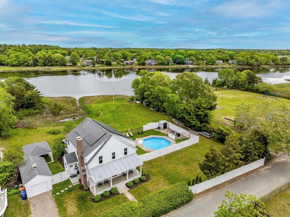 A large house with a swimming pool, surrounded by a well-maintained lawn and a lake.