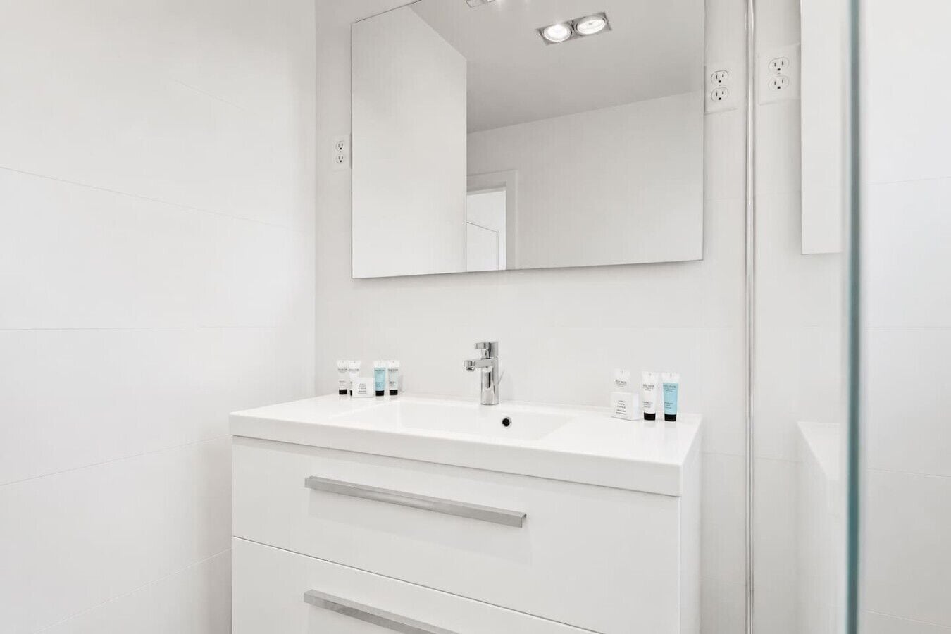 A modern bathroom with a white vanity, a mirror, and two sinks.