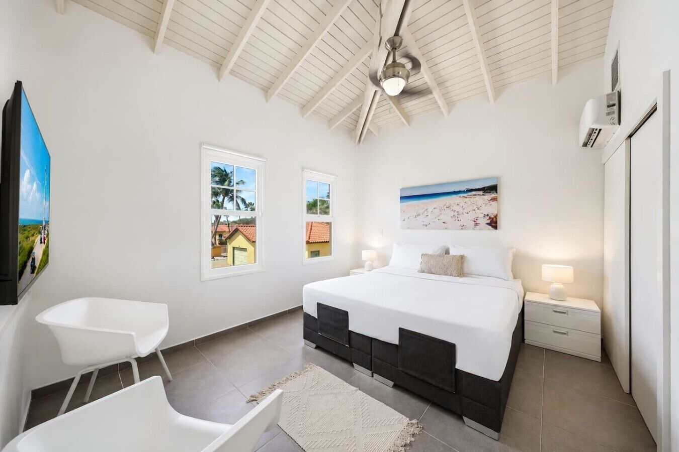A bedroom with a bed, a ceiling fan, a window with a view, a nightstand, and a chair.