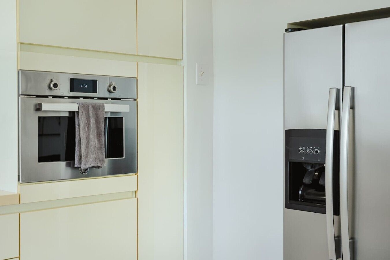 Una cocina con horno de acero inoxidable y refrigerador, un reloj digital y un dispensador de agua.