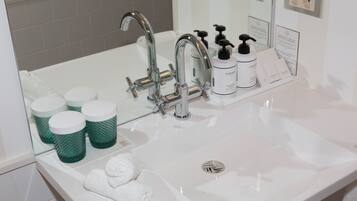 Une salle de bain avec un lavabo blanc, un robinet chromé, des distributeurs de savon verts et un miroir.