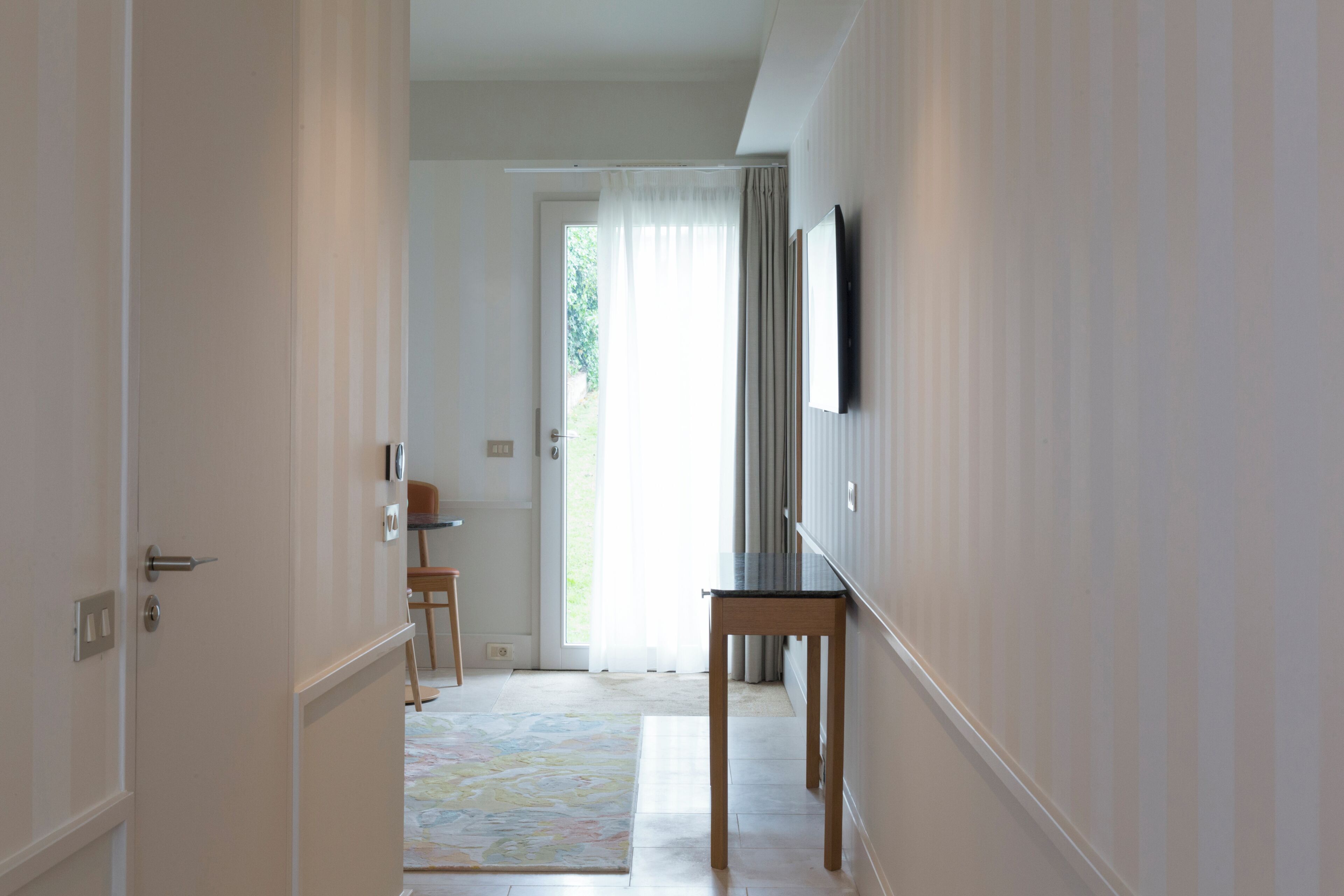 A hallway with a door, a small table, and a television mounted on the wall.