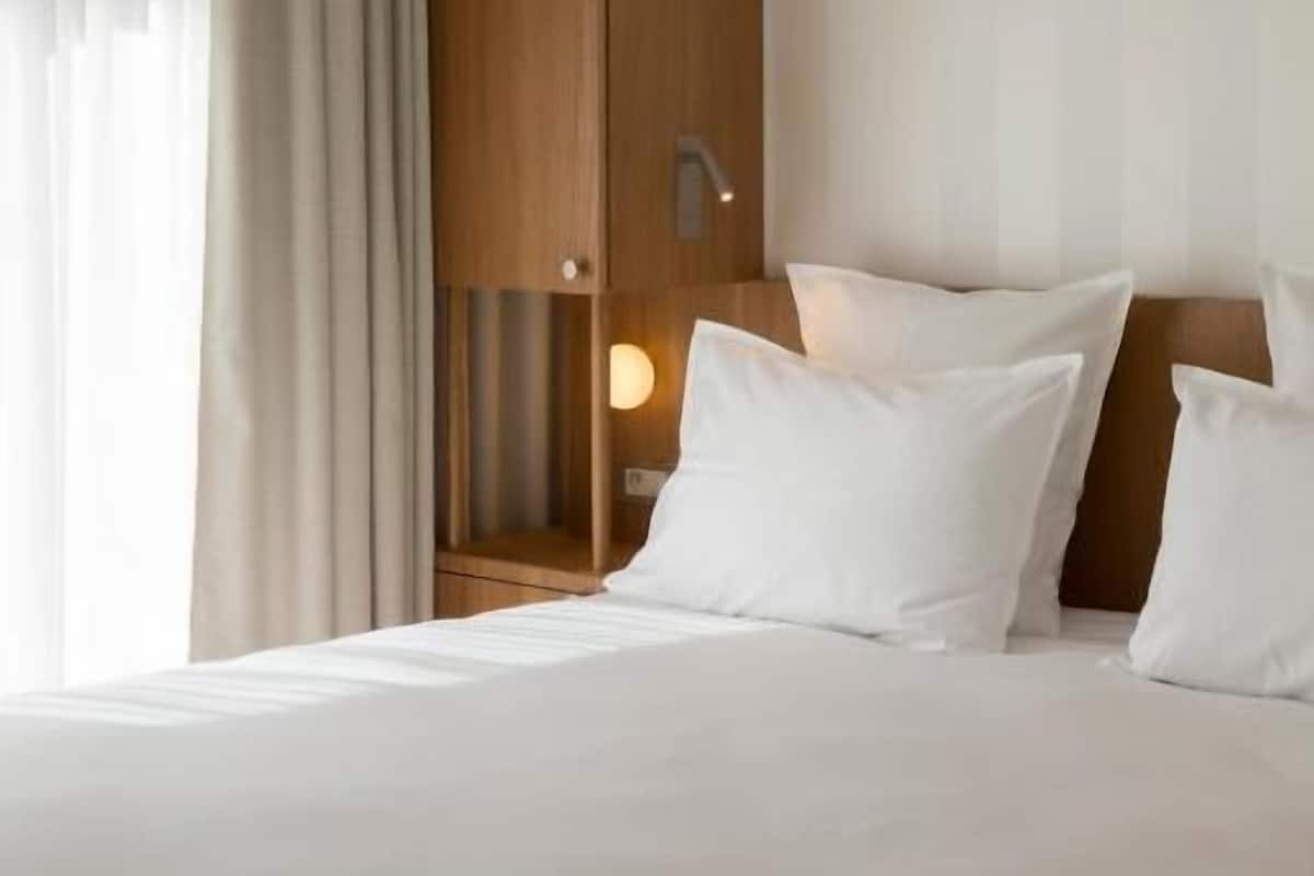 Una habitación de hotel con una cama, un armario de madera, una mesita de noche y una lámpara.