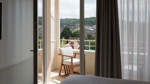 Un balcón con una silla, una cama y vistas a un pueblo.