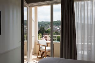 Un balcón con una silla, una cama y vistas a un pueblo.