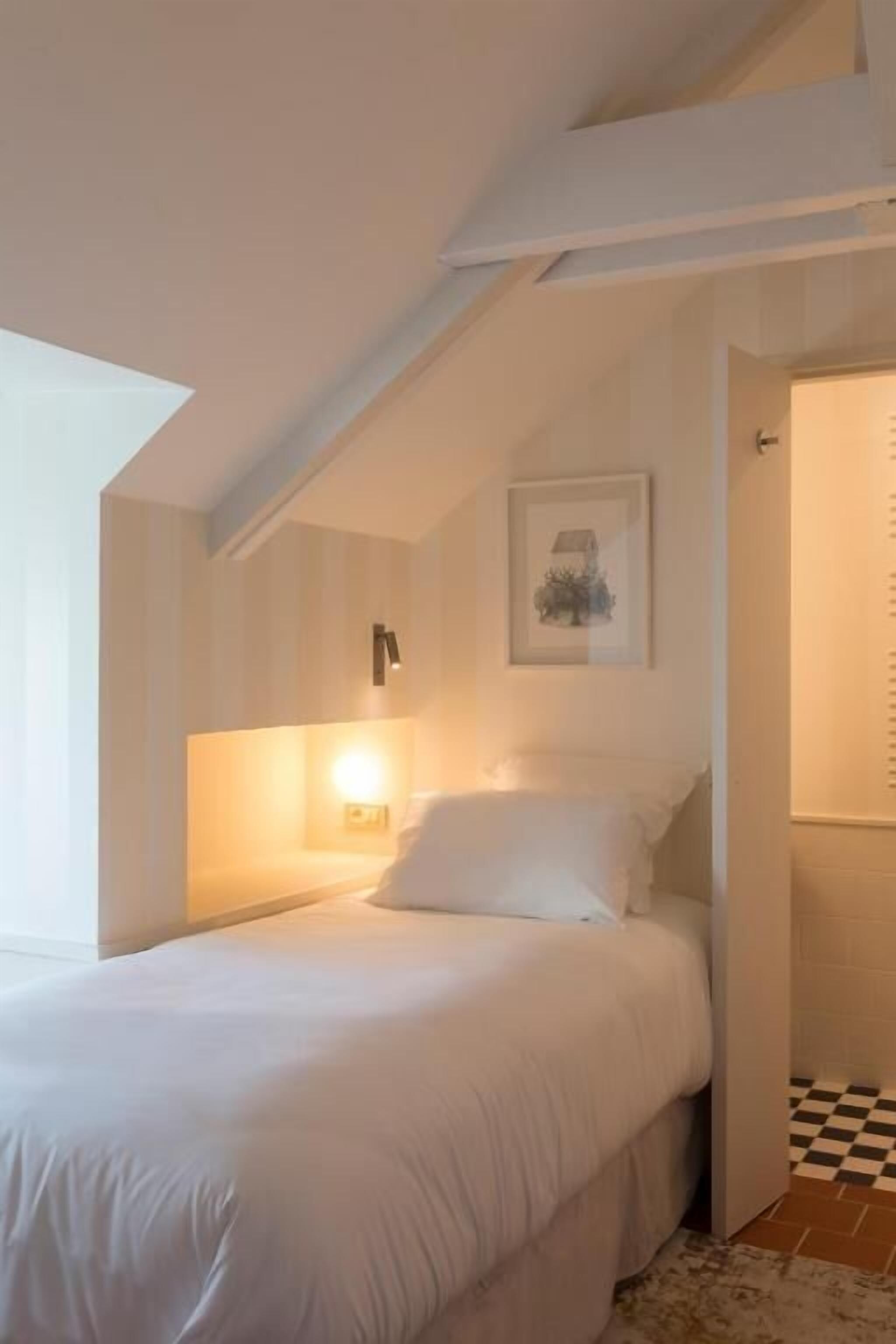 A bedroom with a bed, a wall-mounted light, a framed picture, and a checkered floor.