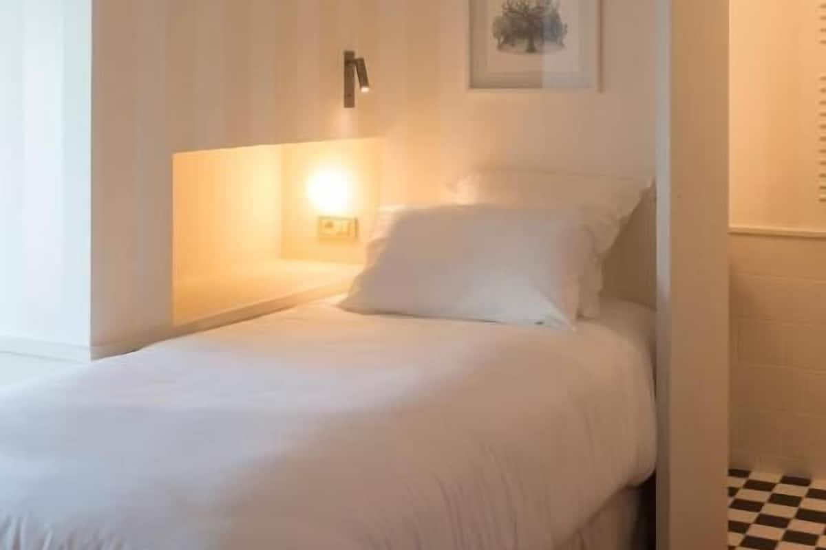 Un dormitorio con cama, una lámpara de pared, un cuadro enmarcado y suelo a cuadros.