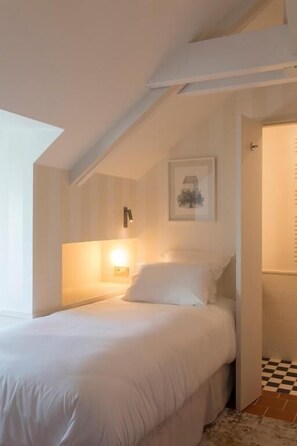 A bedroom with a bed, a wall-mounted light, a framed picture, and a checkered floor. - MAISON BORRÈZE  (Souillac)