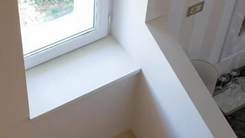 Un rincón de una habitación con una ventana, una pared blanca y una puerta.