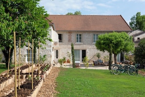 A stone house with a tiled roof, a garden with raised beds, and a bicycle parked outside.