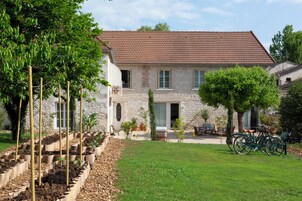 A stone house with a tiled roof, a garden with raised beds, and a bicycle parked outside.