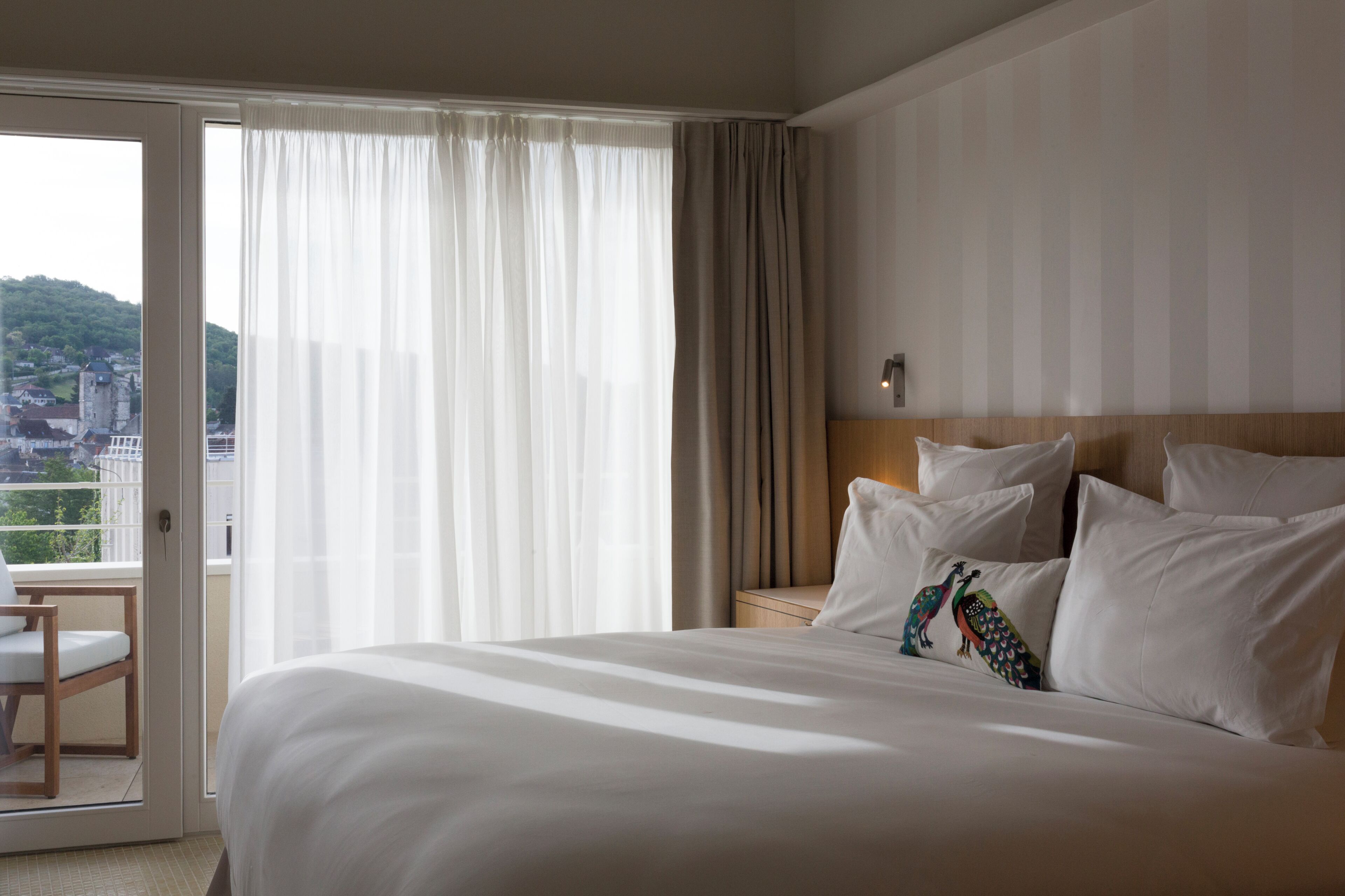 Une chambre d’hôtel avec un grand lit, une table de chevet, une chaise et une vue sur le paysage urbain par la fenêtre.