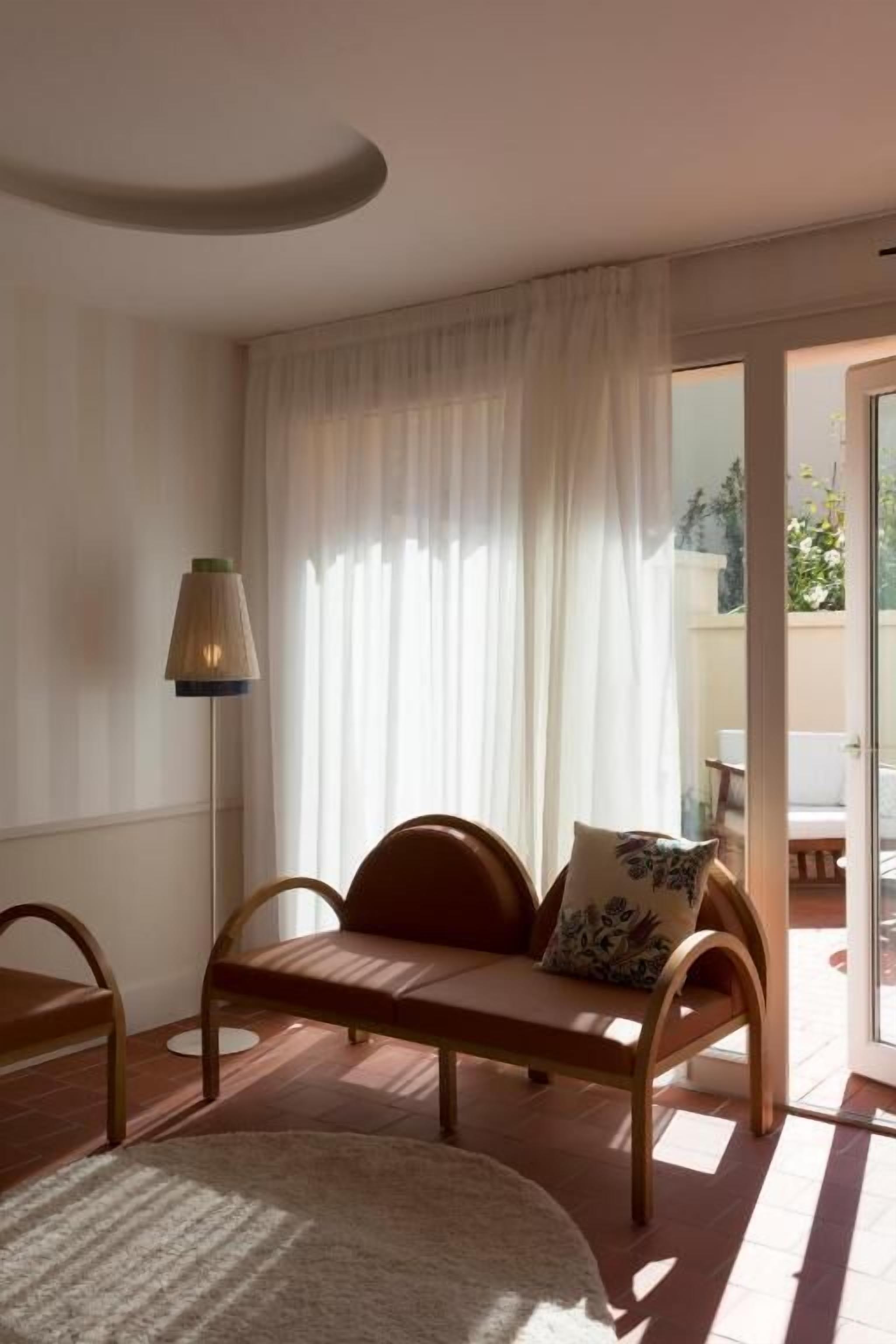 Una habitación con un banco de madera, una lámpara de pie y vistas a un área exterior por un ventanal.