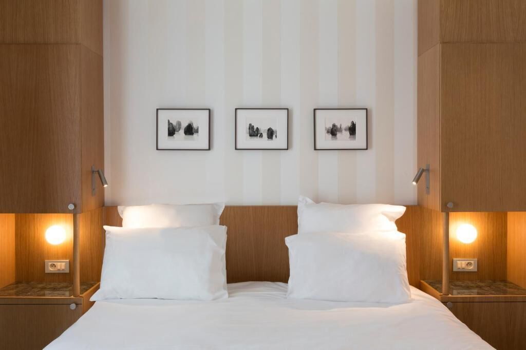 A hotel room with a wooden headboard, a bed with white linens, bedside tables with lamps, and three framed pictures on the wall.