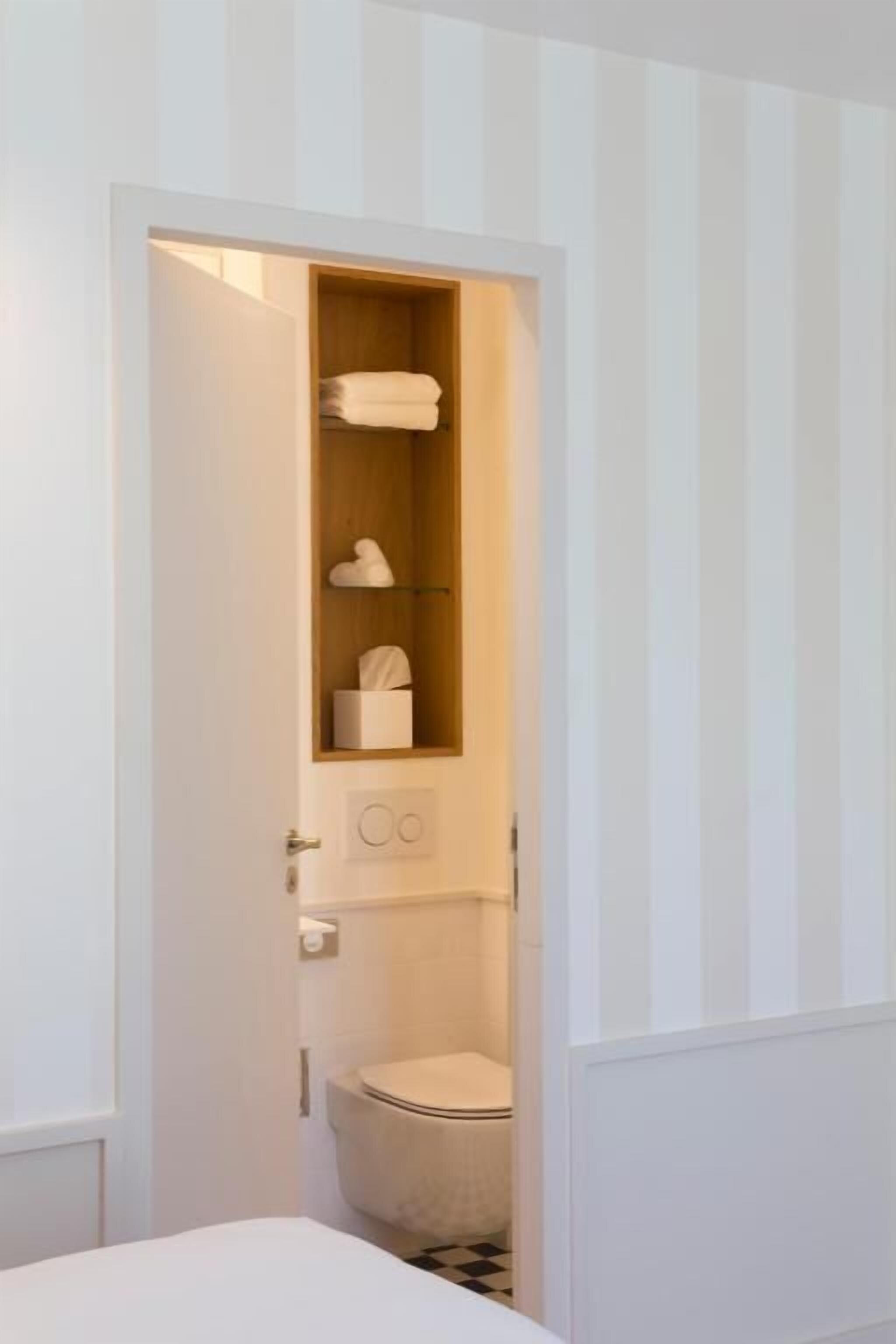 A narrow bathroom with a toilet, a shelf with towels, and a small cabinet.