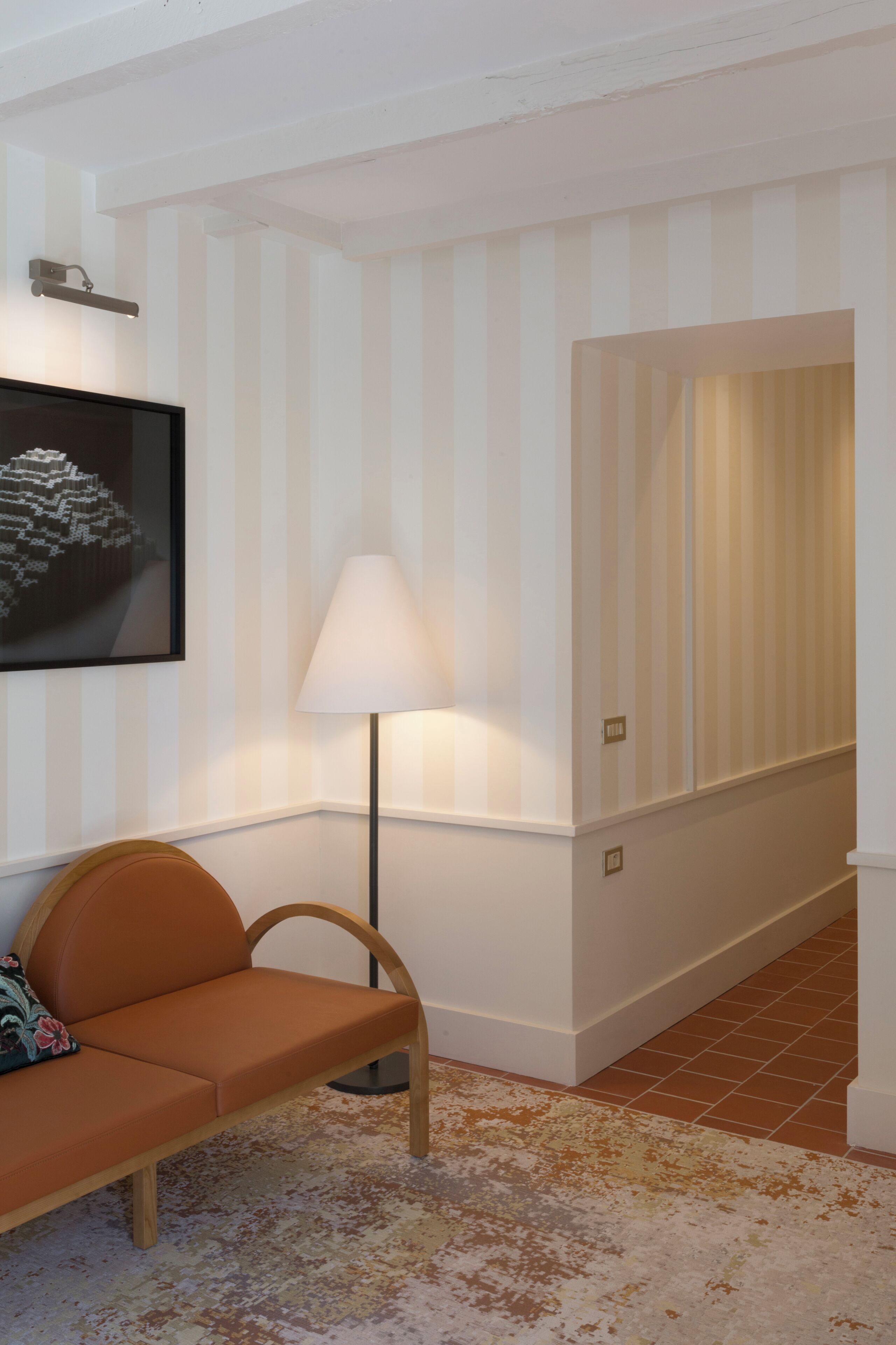 A hallway with striped wallpaper, a lamp, a sofa, and a framed picture on the wall.