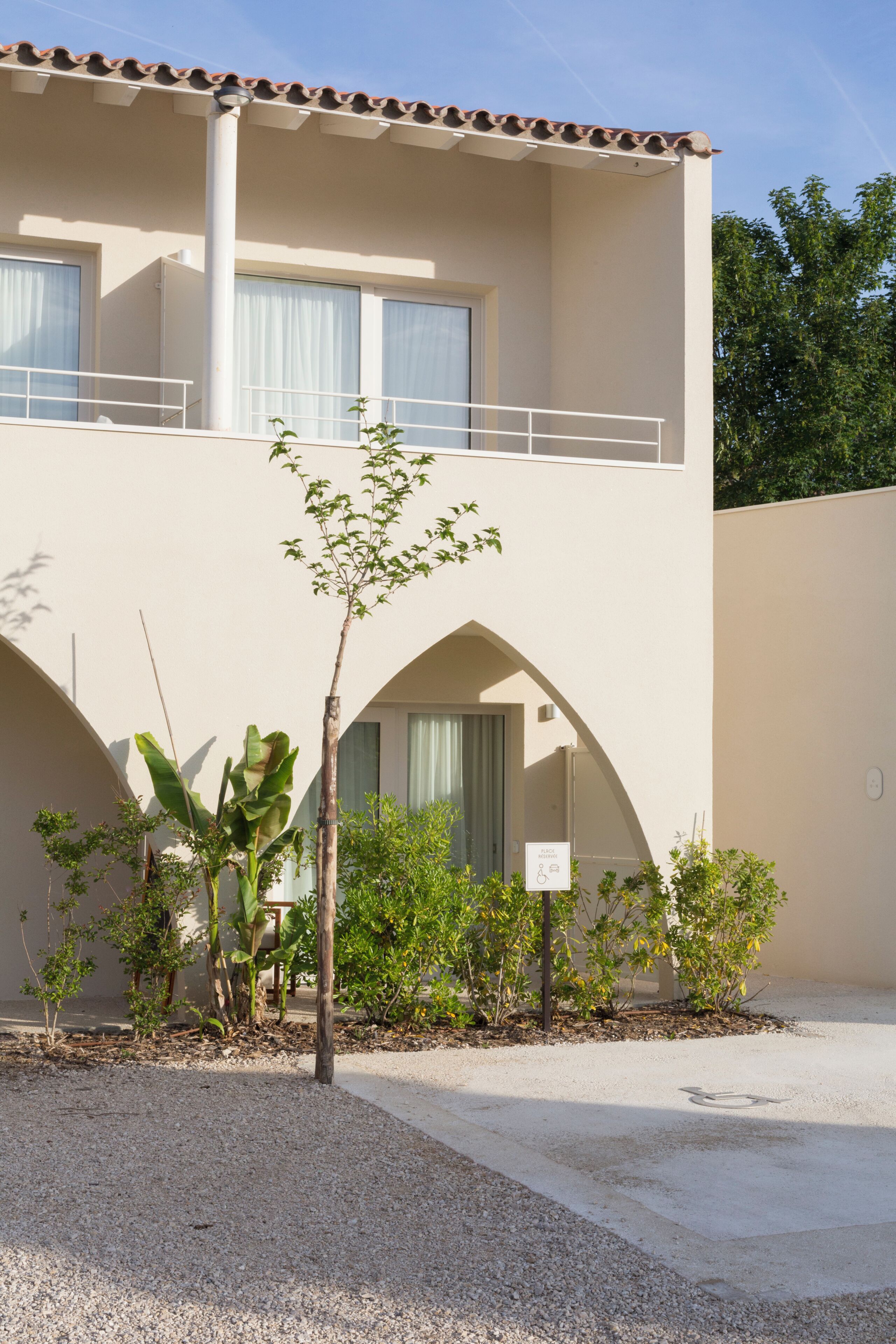 A building with a balcony, a small tree, and a sign indicating a wheelchair-accessible room.