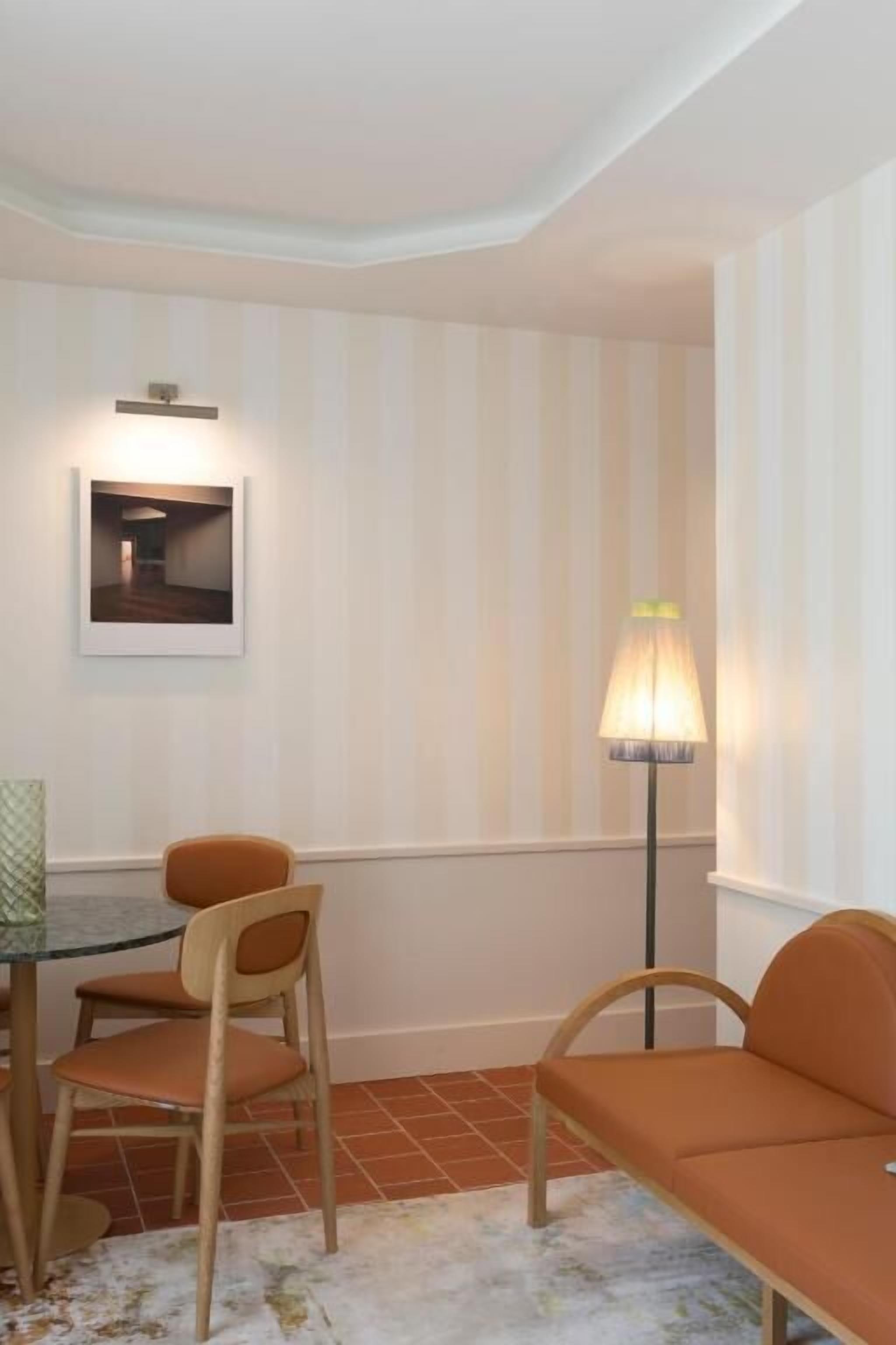 Une pièce comprenant une table à manger, deux chaises, un canapé, un lampadaire et un tableau encadré accroché au mur.