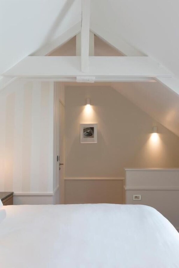 A bedroom with a sloped ceiling, a bed, a nightstand, and a wall-mounted light fixture.