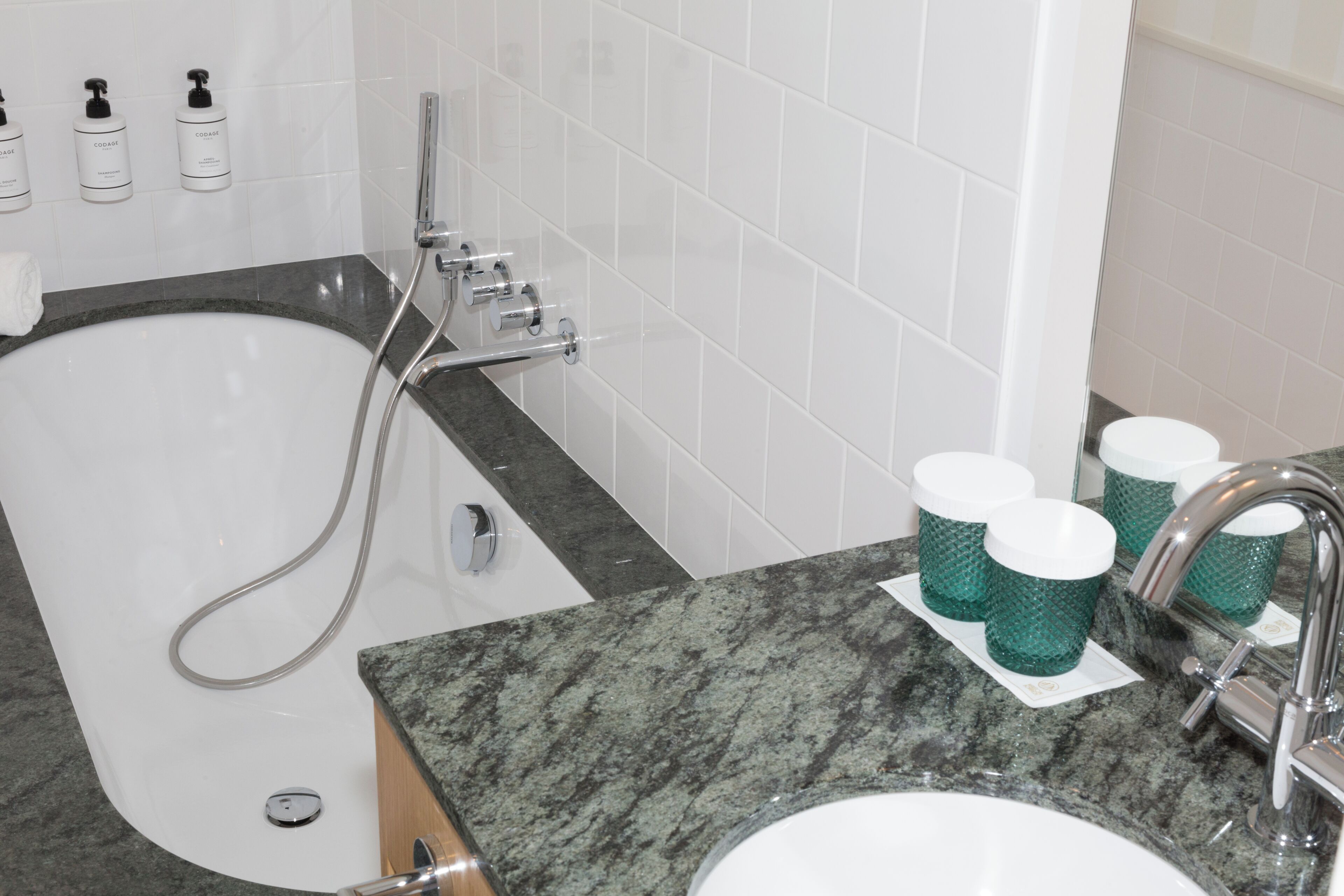 Un baño con bañera, lavamanos y tres tazas verdes sobre el mostrador.