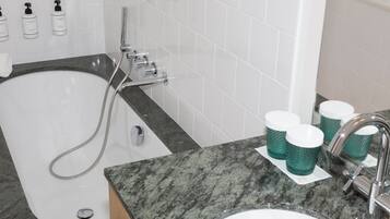 Un baño con bañera, lavamanos y tres tazas verdes sobre el mostrador.