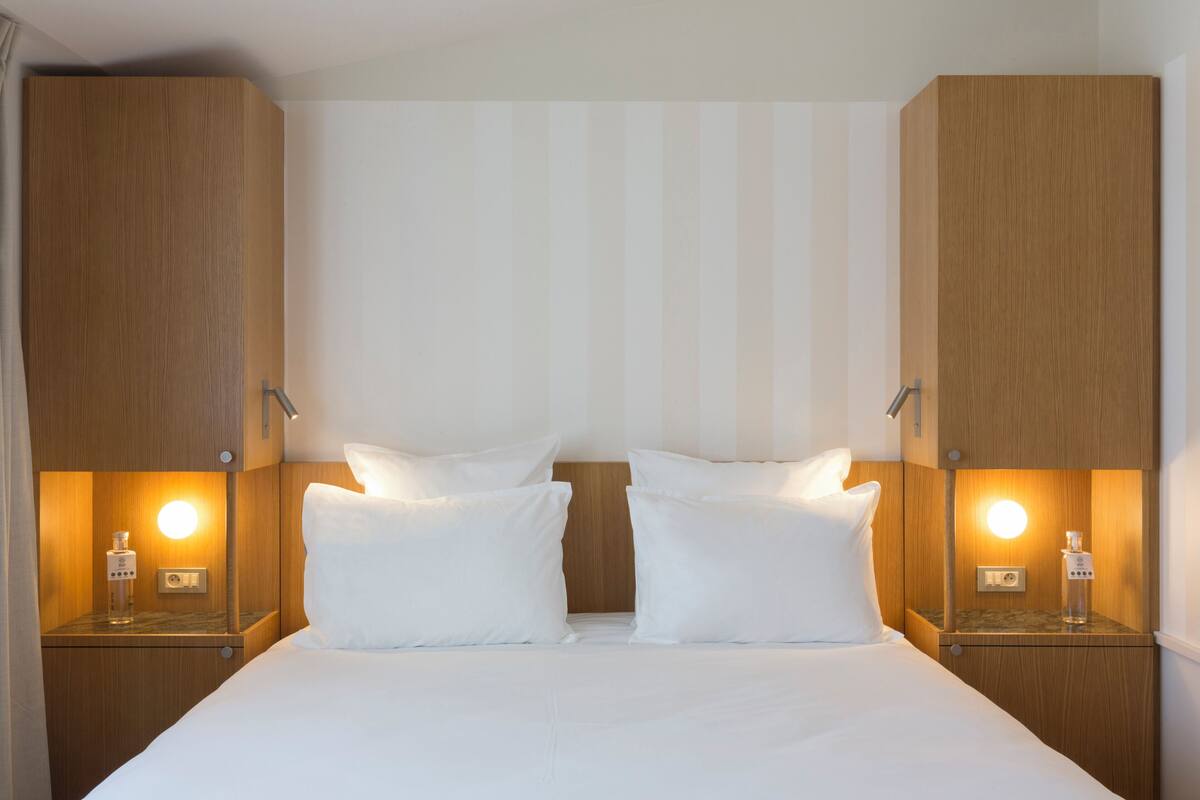 Una habitación de hotel con una cama grande, dos mesitas de noche con lámparas y un cabecero de madera.