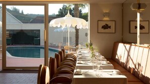 Un comedor con vista a la piscina, una mesa larga dispuesta para comer y un banco a lo largo de la pared.