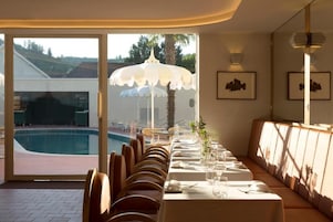 A dining area with a pool view, a long table set for dining, and a bench along the wall.