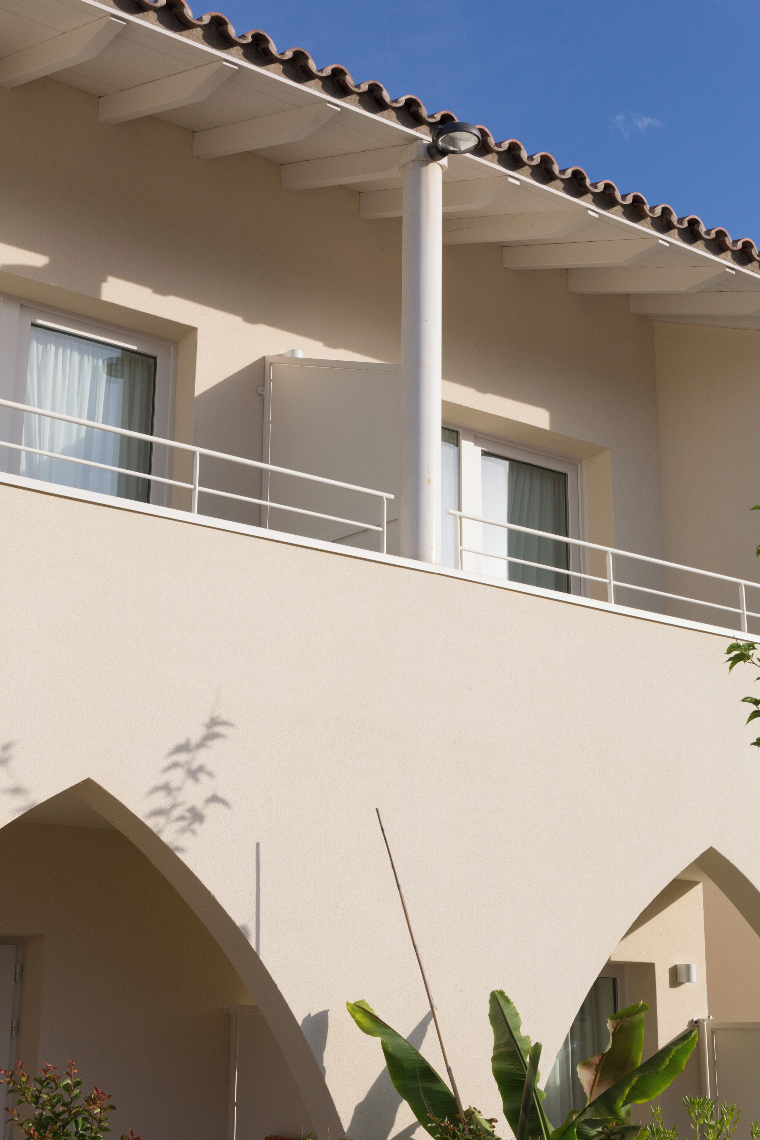 A building with a flat roof, a balcony, and a window with a curtain.