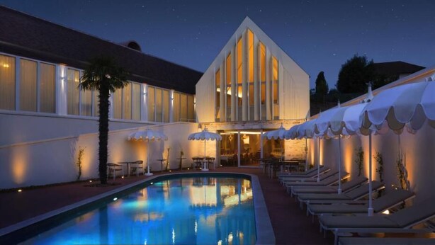 Un hotel con piscina, sillas de descanso y sombrillas.