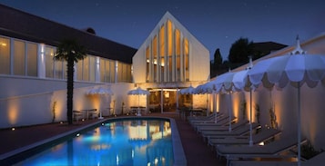 A hotel with a swimming pool, lounge chairs, and umbrellas.