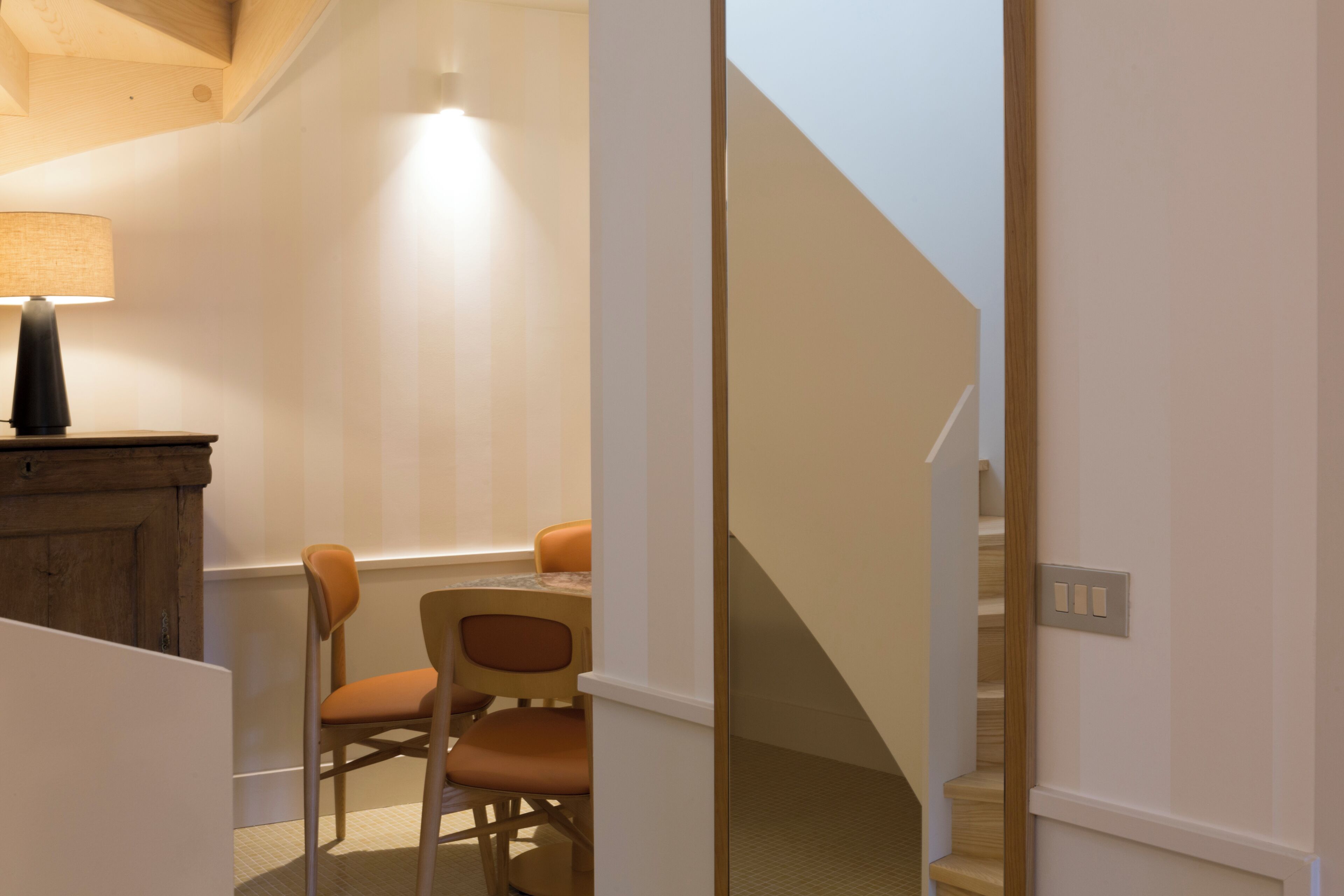 A room with a dining table, chairs, a lamp, and a staircase.