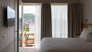 Habitación de hotel con cama, televisor, balcón con una silla y vista a la ciudad.