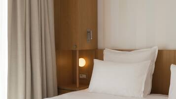 A hotel room with a bed, curtains, a nightstand, and a wall-mounted light.