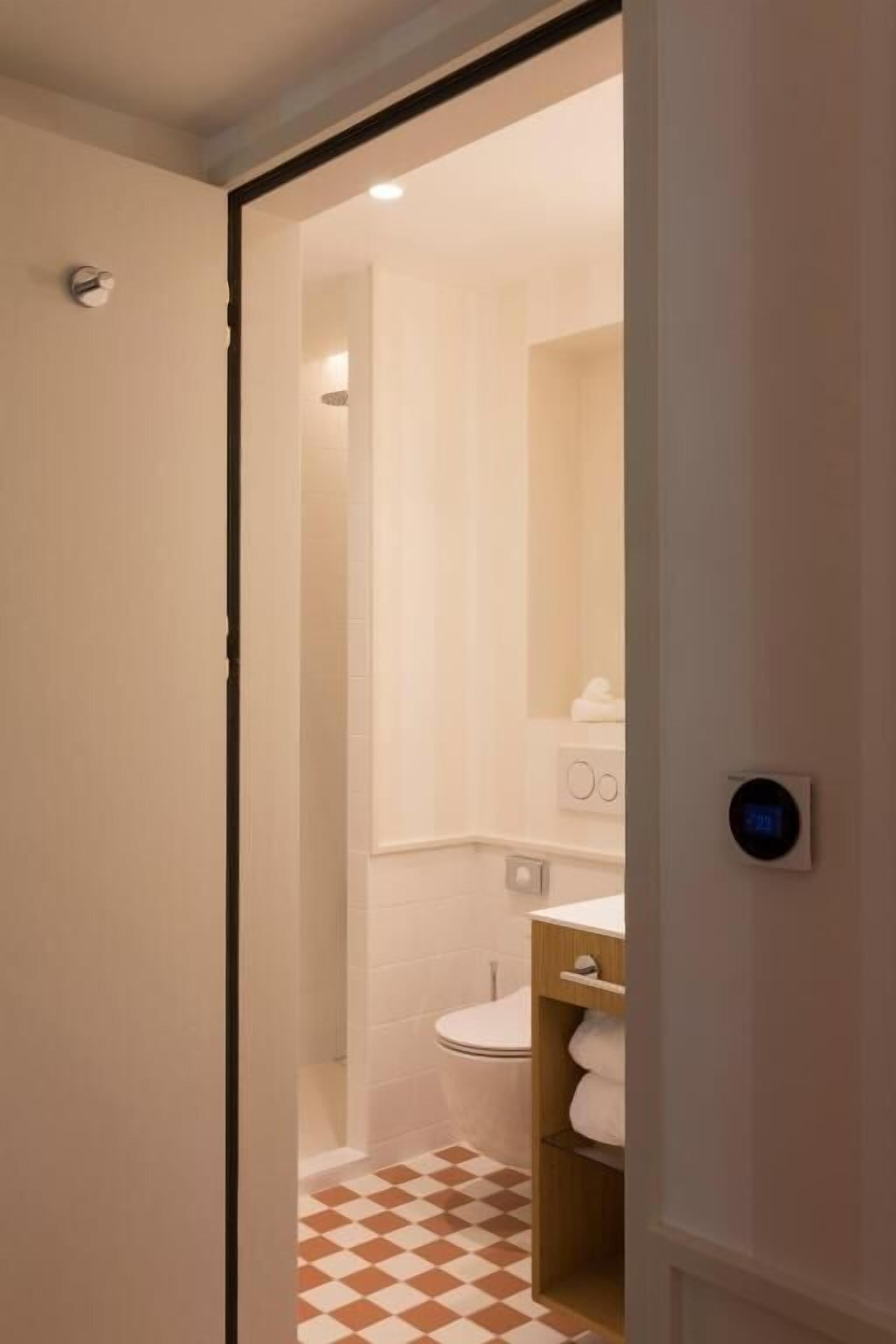 Un baño con inodoro, repisas con artículos de aseo y piso a cuadros.