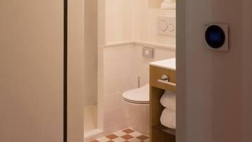 Un baño con inodoro, repisas con artículos de aseo y piso a cuadros.
