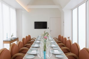 Una taula de dinar llarga amb cadires, un vas amb flors i un televisor de pantalla plana a la paret.