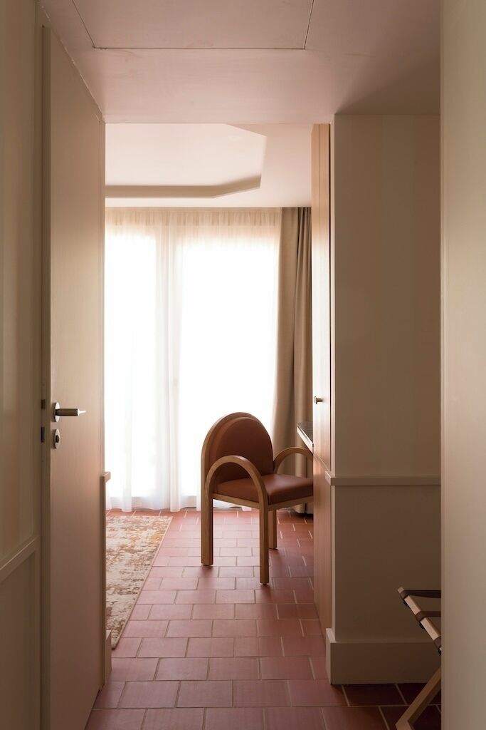 Un couloir avec une chaise en bois, une porte et une fenêtre avec des rideaux.