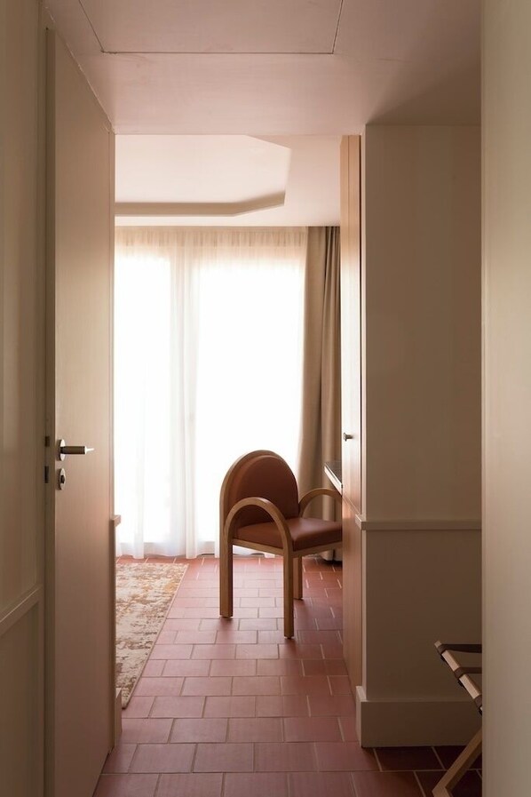 A hallway with a wooden chair, a door, and a window with curtains. - MAISON BORRÈZE (Souillac)