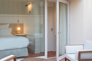 A hotel room with a bed, a nightstand, a chair, and a sliding glass door leading to a balcony.