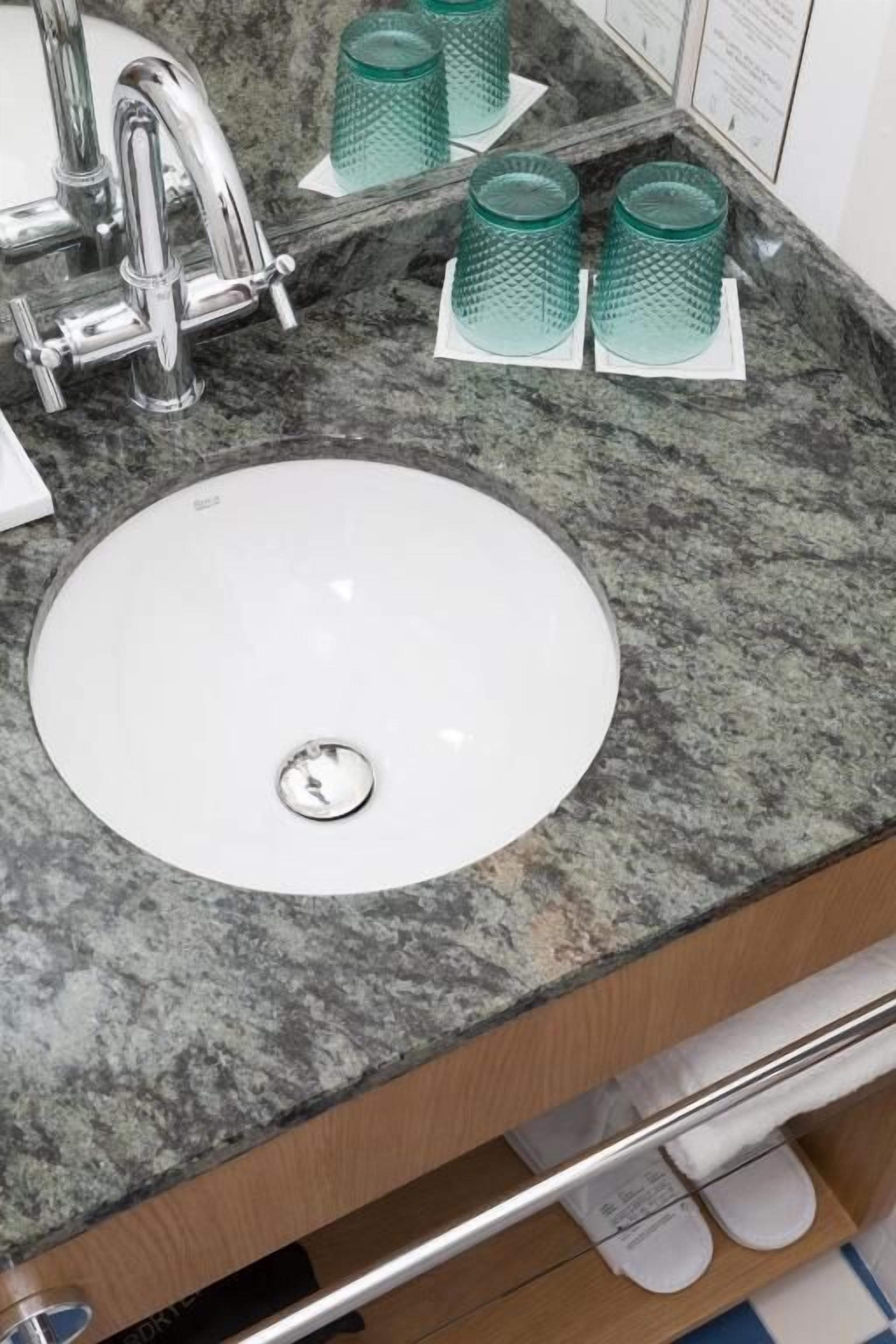 A bathroom with a white sink, a chrome faucet, and green glass tumblers on the countertop.