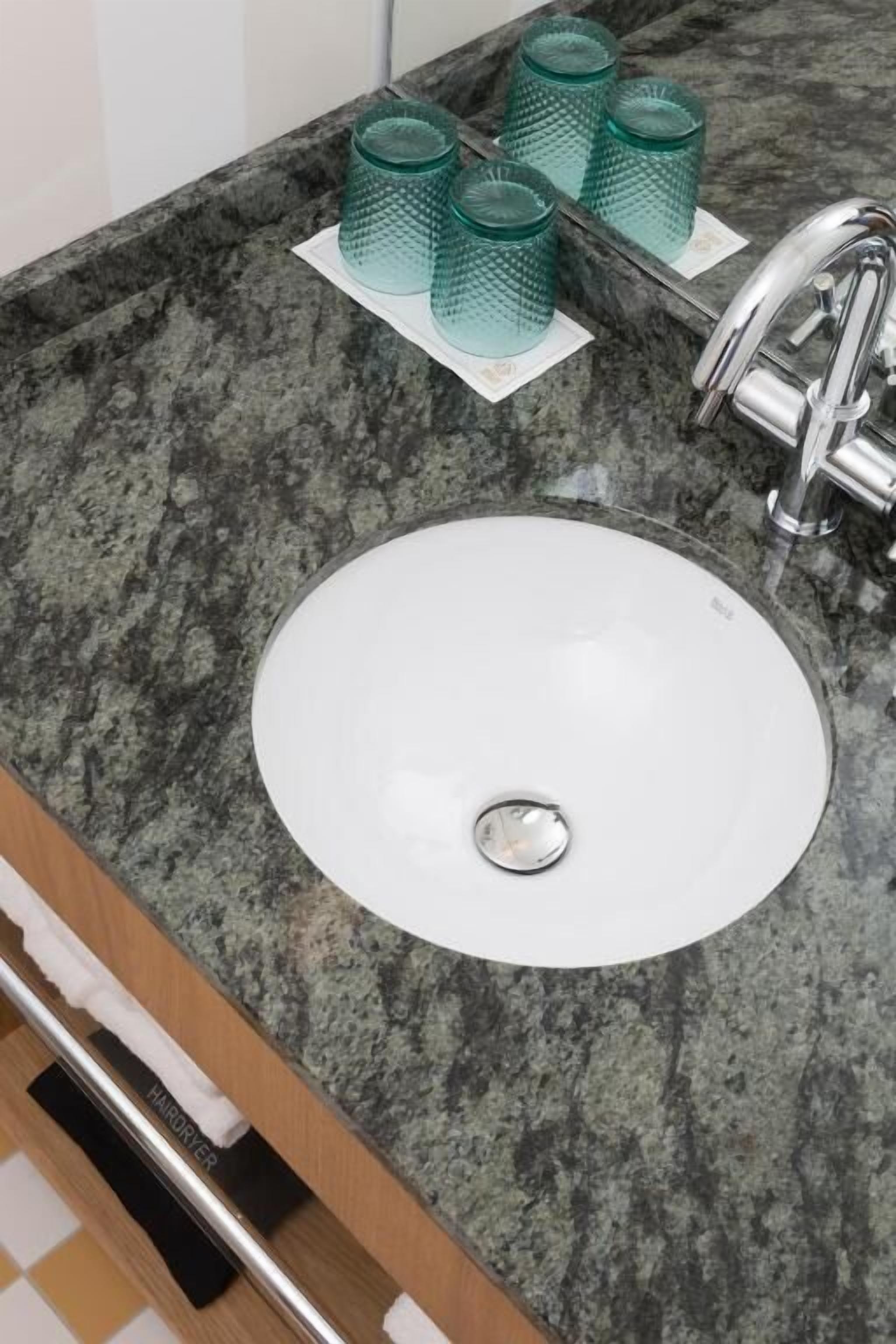 A granite countertop with a white sink and four green glass tumblers.
