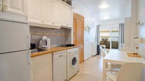 A compact kitchen with white cabinets, a washing machine, and a dining area with a table and chairs.
