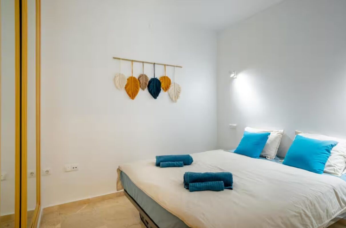 Een slaapkamer met een bed, blauwe handdoeken, wit beddengoed en een wandlamp.