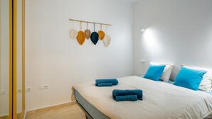 A bedroom with a bed, blue towels, white bedding, and a wall-mounted light fixture.