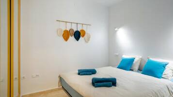 Een slaapkamer met een bed, blauwe handdoeken, wit beddengoed en een wandlamp.