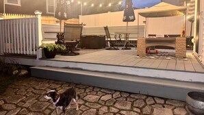 Een terras met buitenmeubilair, een hond en lichtjes.