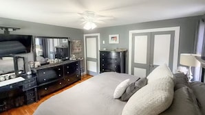 Een slaapkamer met een bed, dressoir, spiegel en plafondventilator.