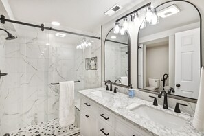 A modern bathroom with a large mirror, two sinks, a shower, and a towel rack.