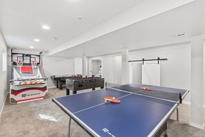 A room with a ping pong table, a foosball table, and a basketball hoop.